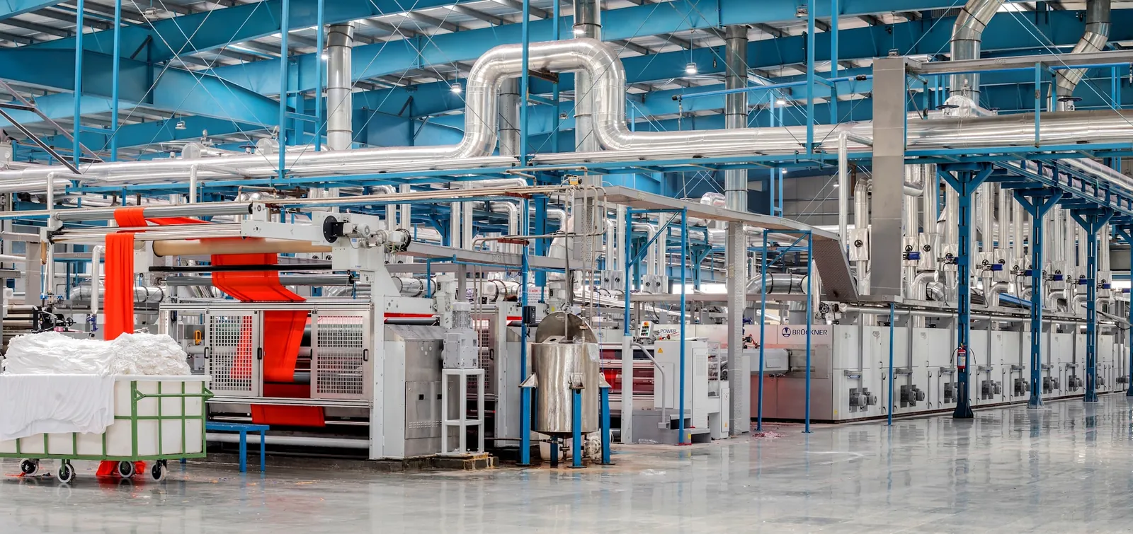 Línea industrial de acabado textil con rollos de tejido y maquinaria